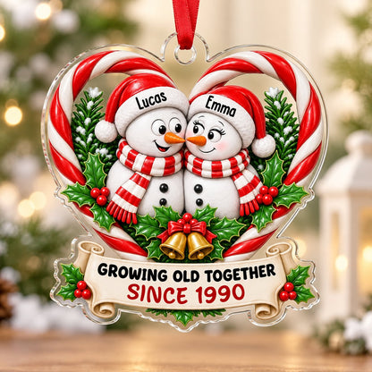 Two snowmen touching noses inside a candy-cane heart with holly, gold bells, and a scroll banner with names and year.