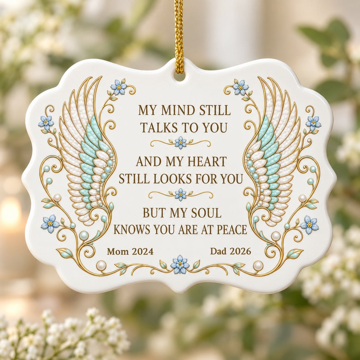 Medallion ceramic ornament with gold-outlined angel wings, blue forget-me-nots, and a memorial quote with name and year.