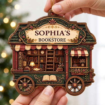 Custom-cut wood ornament shaped like a vintage bookstore wagon with books, ladder, and striped awnings.