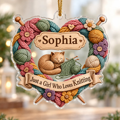Heart-shaped acrylic ornament with yarn wreath, knitting needles, brown cat and "Just a Girl Who Loves Knitting" text.