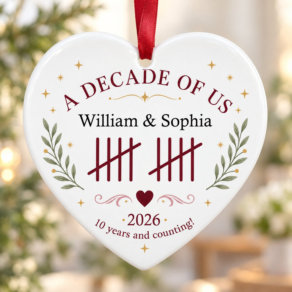 Heart ceramic ornament with 'A Decade of Us', • 2026 •, tally marks, green branches, gold stars, and couple names.