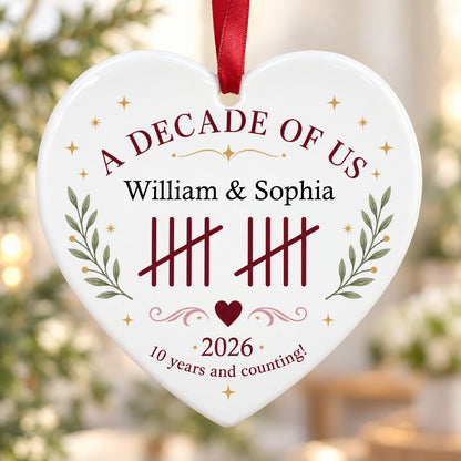 Heart ceramic ornament with 'A Decade of Us', • 2026 •, tally marks, green branches, gold stars, and couple names.