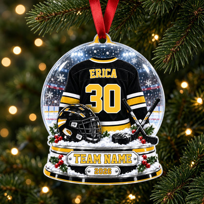 Acrylic snow globe ornament with hockey jersey, helmet, crossed sticks, puck, holly, and a silver plaque base.