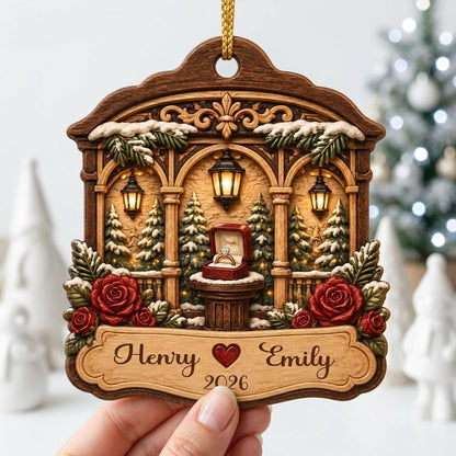 Arched wood ornament with three lanterns, pine trees, red roses, and an open ring box on a central pedestal.