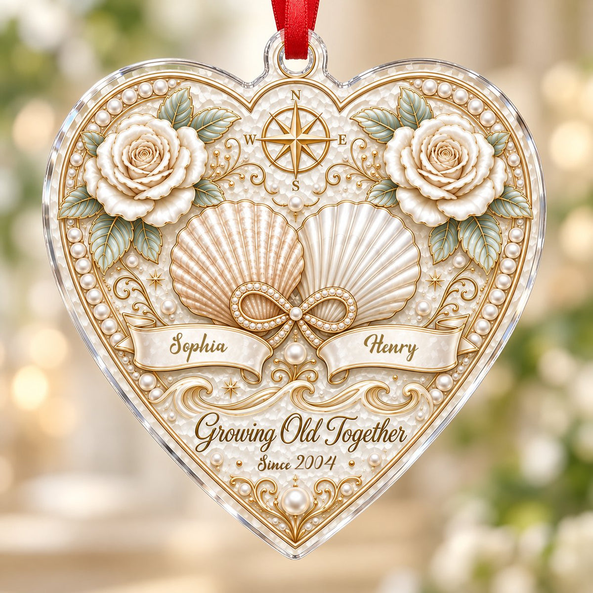 Heart-shaped clear acrylic ornament with seashells, pearl infinity symbol, compass star, and two name ribbons.