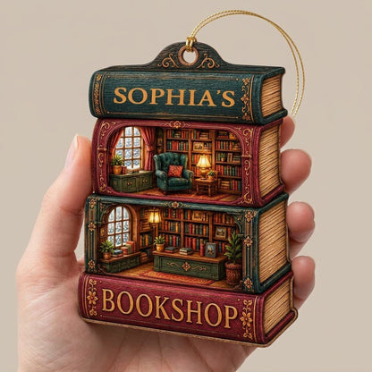 Custom-cut ornament of stacked books showing cozy bookshop rooms, BOOKSHOP text, and a personalized name.