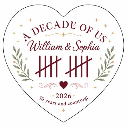 Heart ceramic ornament with 'A Decade of Us', • 2026 •, tally marks, green branches, gold stars, and couple names.