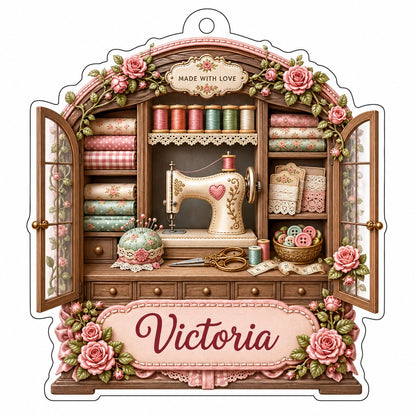 Acrylic ornament shaped like a sewing cabinet with roses, sewing machine, scissors and a pink name banner.