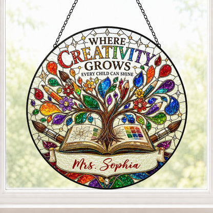 Round stained glass-style suncatcher with tree growing from an open book, paintbrushes, pencils, blossoms, and teacher n