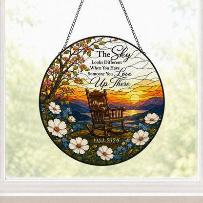 Round stained glass–style suncatcher with an empty rocking chair on a hill at sunset with flowers and a lake.
