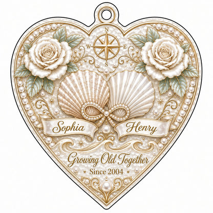 Heart-shaped clear acrylic ornament with seashells, pearl infinity symbol, compass star, and two name ribbons.