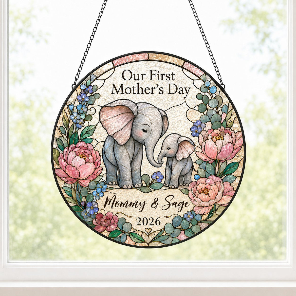 Round stained-glass suncatcher of mother and baby elephants touching trunks amid pink peonies and blue flowers.