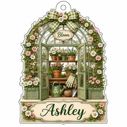 Arched acrylic ornament of a green greenhouse with daisy bow, flowers, tools, and 'Bloom' with a personalized name.