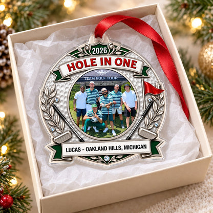 Silver trophy-style golf ornament with laurel branches, crossed clubs, red flag, 2026 and HOLE IN ONE, plus a circular p